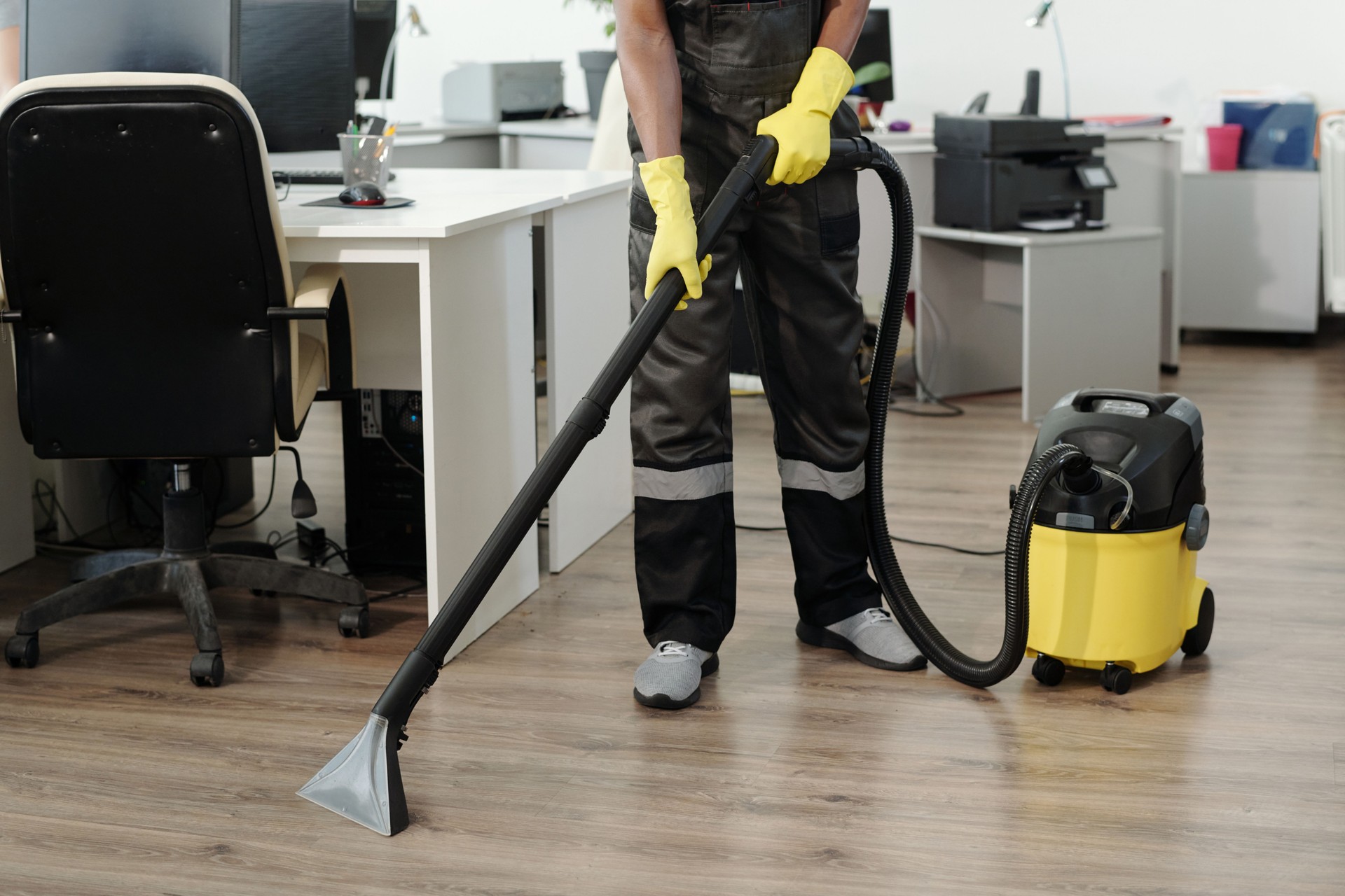 Young black man in uniform and yellow gloves using vacuum cleaner